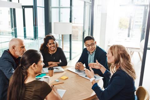 Imagen de dos hombres y tres mujeres de diferentes orígenes, sentados en una mesa de conferencias.